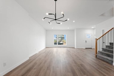 Büyük, boş bir oturma odası ve tavandan sarkan siyah bir avize. Oda temiz, modern görünümlü ve aydınlık.