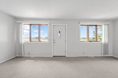 Büyük, boş bir oturma odası, kapısı ve iki penceresi var. Kapı beyaz ve gözetleme deliği var. Pencereler geniş ve dışarıdan bir manzara sağlıyor. Oda temiz ve dağınık.