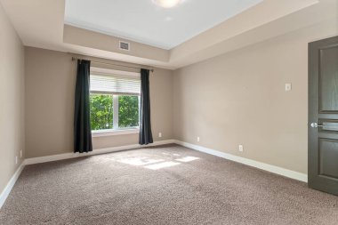 Penceresinde siyah perde olan büyük, boş bir oda. Oda çıplak ve dağınık, açık renk düzeniyle.