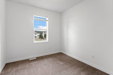 Penceresi ve beyaz duvarı olan küçük bir yatak odası. Oda boş ve basit, temiz bir görünüşü var.