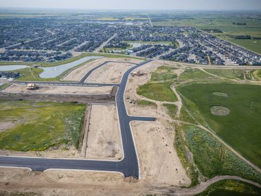 İnşaat halindeki bir yolu olan bir yerleşim yeri manzarası. Yol çimenler ve ağaçlarla çevrili.