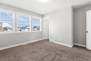 Büyük, beyaz kapısı ve üç penceresi olan boş bir oda. Oda çok temiz ve nötr bir renk düzeni var.