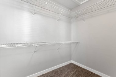 Beyaz bir duvarı ve beyaz zemini olan beyaz bir dolap. Dolap boş ve askılarda hiç giysi yok.