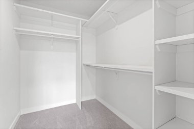 Raflı ve askılı beyaz dolap. Dolap boş ve duvarlar beyaz.