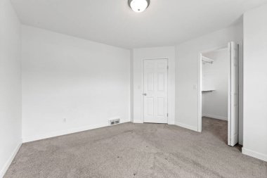 Beyaz kapısı ve beyaz dolabı olan beyaz bir oda. Oda boş ve minimalist bir görünüşü var.