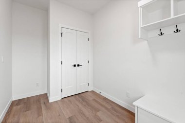 Beyaz kapısı ve beyaz duvarı olan beyaz bir oda. Oda boş ve ahşap zemini var.