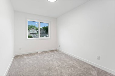 Penceresi ve halısı olan beyaz bir oda. Oda boş ve minimalist bir görünüşü var.