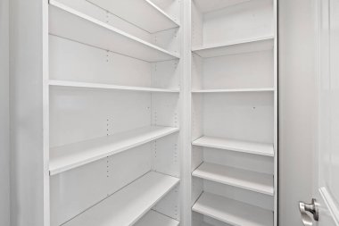 Rafları ve kapısı olan beyaz bir kiler. Kiler boş ve temiz. Kapı açık ve ışık açık.