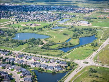 Ortasında büyük bir gölet olan yerleşim yeri manzarası. Gölet ağaçlar ve evlerle çevrili.