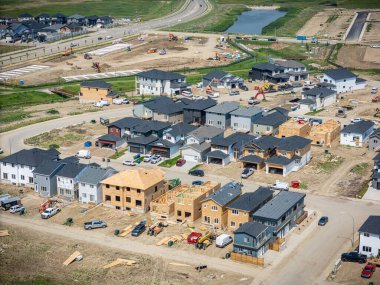Arkasında bir sürü ev olan bir inşaat alanı. Evler inşa ediliyor ve bölgede çok sayıda kamyon ve inşaat ekipmanı var.