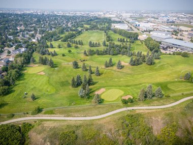 Yeşil çimenli bir arazisi ve yolu olan golf sahası. Golf sahası ağaçlar ve evlerle çevrili.