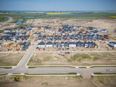 Evleri ve caddeleri olan bir yerleşim yeri. Evlerin çoğu beyaz ve caddeye park etmiş birkaç araba var.