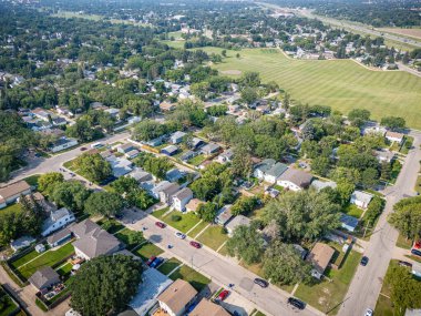 Evleri ve ağaçları olan bir yerleşim yeri. Evlerin çoğu beyaz ve caddeye park edilmiş arabalar var.