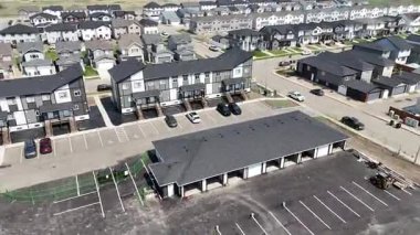 Birçok evi ve dairesi olan bir yerleşim yeri. Evlerin çoğu beyaz ve siyah. Otoparkta park etmiş bir sürü araba var.