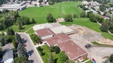 Okul yukarıdan gösteriliyor, arka planda büyük yeşil bir alan var. Okul evler ve ağaçlarla çevrili ve garaj yolunda park edilmiş arabalar var. Toplum kavramı ve barışçıl