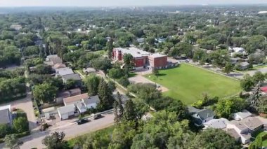 Okul ve arka planda evler olan bir şehir caddesi. Gökyüzü bulutlu ve atmosfer sakin.