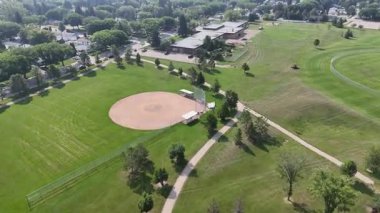 Beyzbol sahası ve yolu olan bir park. Çimler yeşil ve ağaçlar uzun.