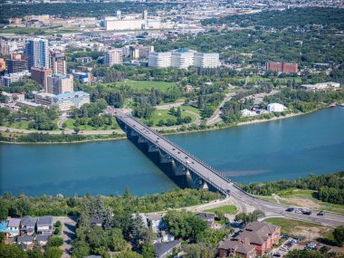 Nehrin üzerinde köprüsü olan şehir manzarası. Köprü ağaçlar ve evlerle çevrilidir. Şehir hareketlilikle dolup taşıyor ve nehir sakin ve huzurlu.