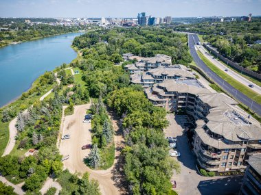 Nehir ve yol olan şehir manzarası. Yol arabalar ve kamyonlarla dolu. Evler uzun ve otoparkta park edilmiş bir sürü araba var.