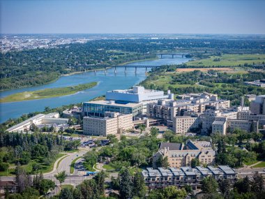Şehir manzarası, içinden nehir akıyor ve ortasında büyük bir hastane var. Hastane ağaçlar ve binalarla çevrili.