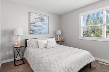 Beyaz yataklı ve beyaz duvarlı bir yatak odası. Yatak beyaz bir yorgan ve yastıkla kaplı. Komodinin üzerinde iki lamba var. Odanın temiz ve basit bir tasarımı var.