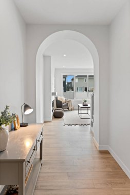 Koridorda ışıklı bir masa ve arka planda bir kanepe var. Koridor beyaz ve kanepe kahverengi.