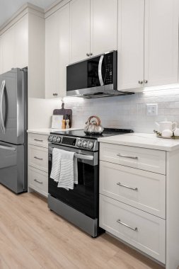 Siyah ocağı ve gümüş buzdolabı olan bir mutfak. Soba yanıyor ve üzerinde bir havlu asılı.