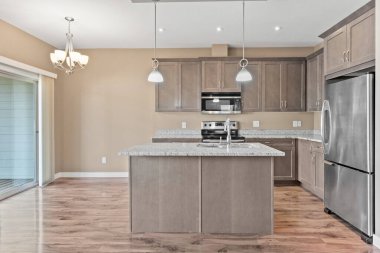 Paslanmaz çelik buzdolabı, mikrodalga fırın ve lavabosu olan bir mutfak. Tezgah granitten yapılmış ve dolaplar ahşaptan yapılmış. Mutfak boş ve temiz.