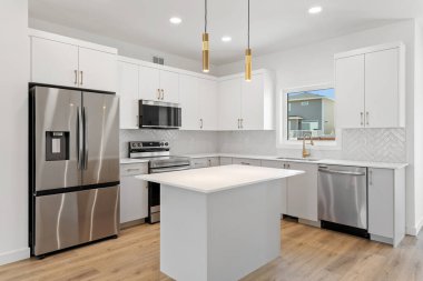 Beyaz bir adası ve paslanmaz çelik aletleri olan bir mutfak. Mutfak temiz ve iyi düzenlenmiş.