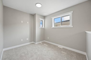 Beyaz bir duvarı ve beyaz halısı olan çok temiz ve boş bir oda. Odada pencere ve lamba var.