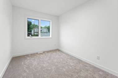 Büyük bir penceresi ve halısı olan beyaz bir yatak odası. Oda boş ve minimalist bir görünüşü var.