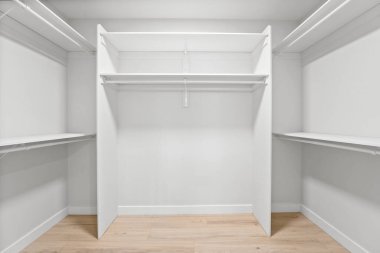 İki rafı ve kapısı olan beyaz bir dolap. Dolap boş. Ahşap bir zemin var.