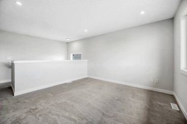Large, empty room with a white wall and a grey carpet. The room is bare and uncluttered, with no furniture or decorations. The white wall and carpet give the room a clean and minimalist look