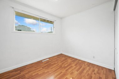 Small bedroom with a window and a wooden floor. The room is empty and has a white wall