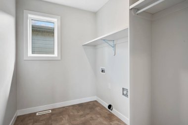 Small, empty laundry room with a window and a white wall. The room is bare and uncluttered, with no furniture or decorations. The window lets in natural light, creating a bright and airy atmosphere