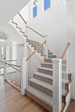 Staircase with a wooden railing and a carpeted landing. The staircase is white and the railing is brown