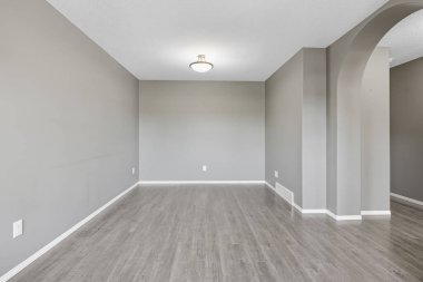 Large, empty room with a white wall and a light fixture. The room is bare and uncluttered, with no furniture or decorations. The space feels open and airy, with a sense of emptiness and potential