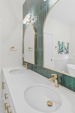 The bathroom is decorated with a green tile wall and gold fixtures. The sink is white and has a gold faucet