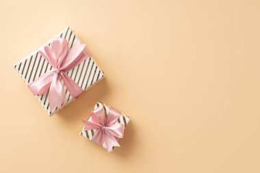 Yeni yıl konsepti. İzole edilmiş açık bej arkaplan üzerinde pembe kurdele yayları olan şık mevcut kutuların üst görünüm fotoğrafı