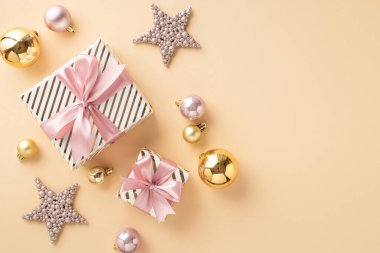 Noel arifesi kavramı. Pembe kurdeleli şık hediye kutularının en üst görüntüsü ışıltılı yıldız süsleri, izole edilmiş açık bej arka planda altın ve pembe mücevherler.