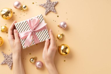Noel konsepti. Kızın ellerinin pembe kurdeleli hediye kutusunu tutarken çekilmiş ilk fotoğraf yıldız süslerinin üzerinde pembe mücevherler, izole edilmiş pastel bej arka planda, kopyalanmış pastel bej bir konfeti.