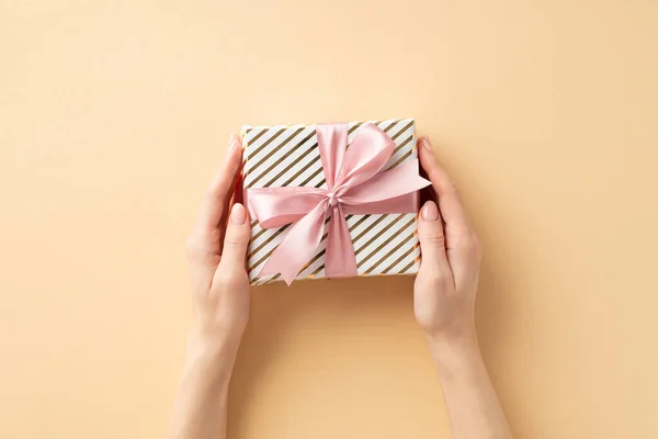 新年的概念 第一人称头像照片妇女的手拿着时髦的礼品盒与粉红缎带弓孤立的灰米色背景 — 图库照片
