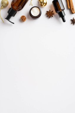 Kış cilt kozmetik konsepti. Kehribar cam şişelerin dikey fotoğrafı krem kavanoz Noel süsleri altın takılar tarçın çubukları ve izole beyaz arka planda anason boş alan