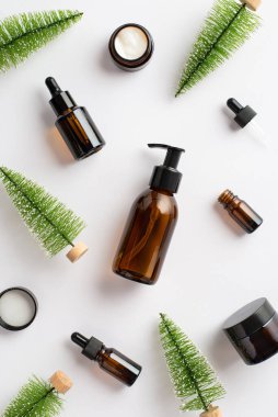 Doğal kozmetik konsepti. Kehribar cam pompa şişesi, krem kavanoz şişeleri ve izole edilmiş beyaz arka planda noel ağacı oyuncaklarının dikey resmi.