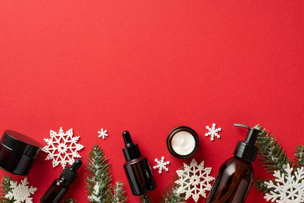 stock image Winter skin care cosmetics concept. Top view photo of amber pump bottle cream jars dropper bottles pine branches in hoarfrost and snowflakes on isolated red background with empty space