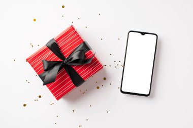 Kara Cuma alışveriş konsepti. Akıllı telefon kırmızı hediye kutusunun üst görüntüsü kurdele yayı ve altın parıltılı konfeti ile izole edilmiş beyaz arka planda