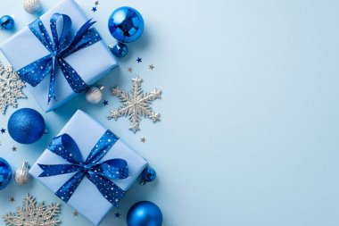 Noel kutlaması kavramı. Moda hediye kutularının üst görüntüsü kurdeleli mavi ve gümüş takılar kar tanesi süslemeleri ve tenha pastel mavi arka planda boş alan konfetileri