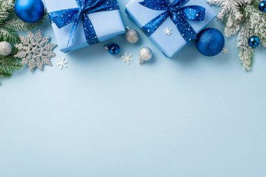 Noel arifesi kavramı. Mavi ve gümüş renkli fiyonklu hediye kutularının üst görüntüsü kar tanesi süslemeleri kardaki çam dalları ve izole edilmiş pastel mavi arka planda boş alan konfetileri.