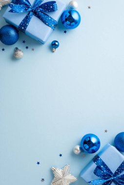 Yeni yıl konsepti. En üstteki görüntüde büyük hediye kutularının dikey fotoğrafı kurdele yayları mavi gümüş mücevherler parlayan yıldız süsü ve izole edilmiş pastel mavi arka planda boş alan üzerine konfeti.