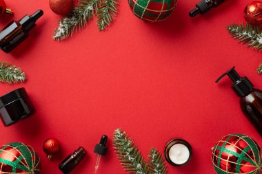 Kış cilt kozmetik konsepti. Noel dekorunun en üst görüntüsü kırmızı ve yeşil takılar kehribar kozmetik şişeler ve ayazda çam dalları izole edilmiş kırmızı arka planda ve ortasında kopyalanmış boşluk